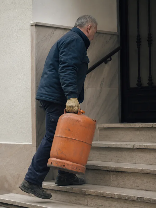 Repartidor subiendo una bombona de gas por la escalera de un portal