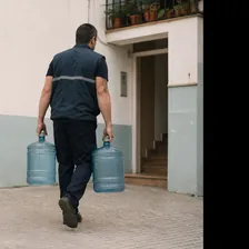 Repartidor llevando dos botellones de agua hacia el portal de un edificio
