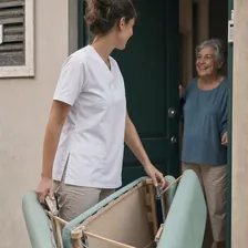 Fisioterapeuta con uniforme y camilla siendo recibida en la puerta de una clienta