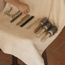 Tijeras, peines y cepillos redondos colocados sobre una toalla en casa de una clienta